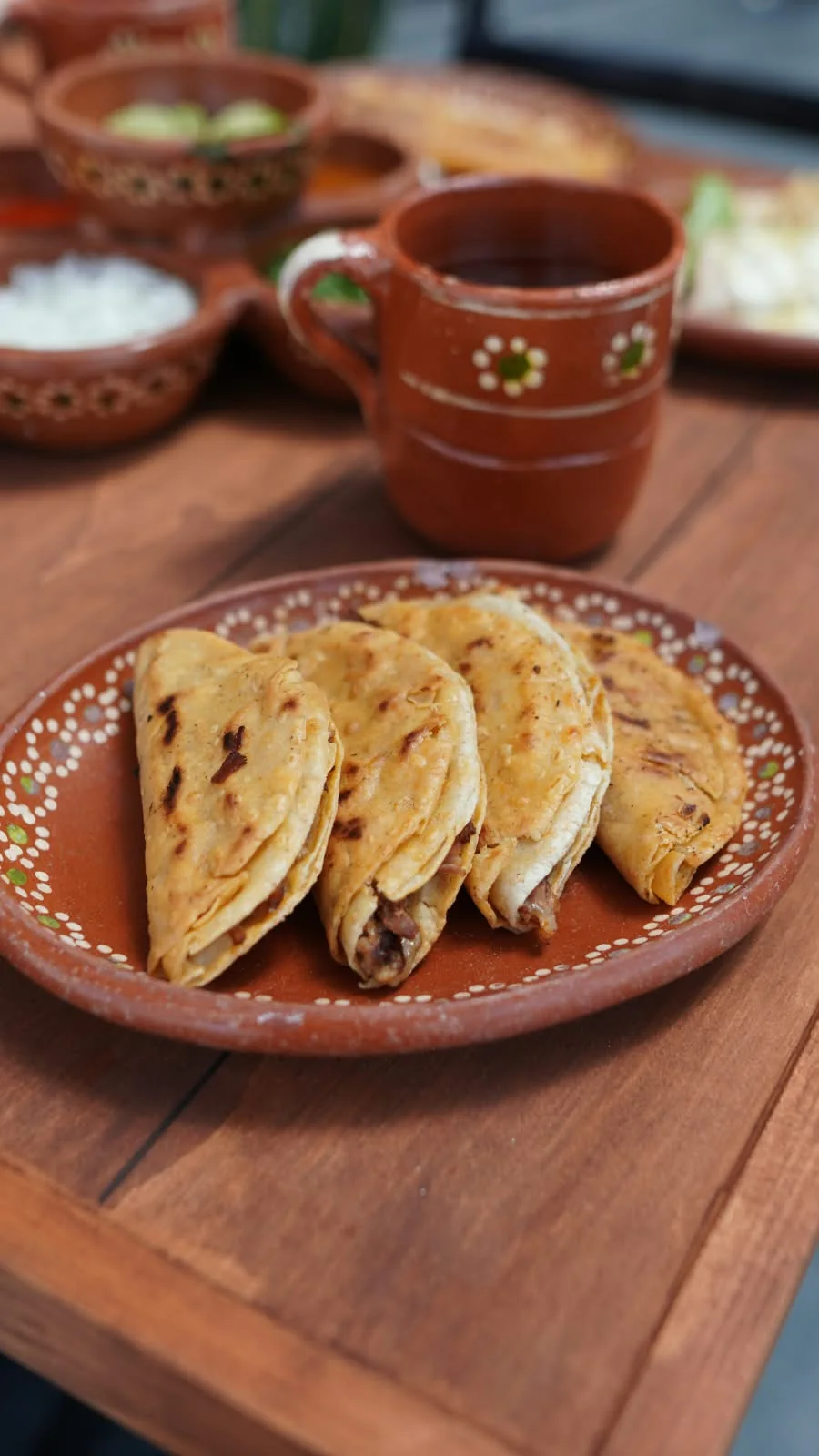 Tacos dorados en plato de barro, con una taza de consomé.