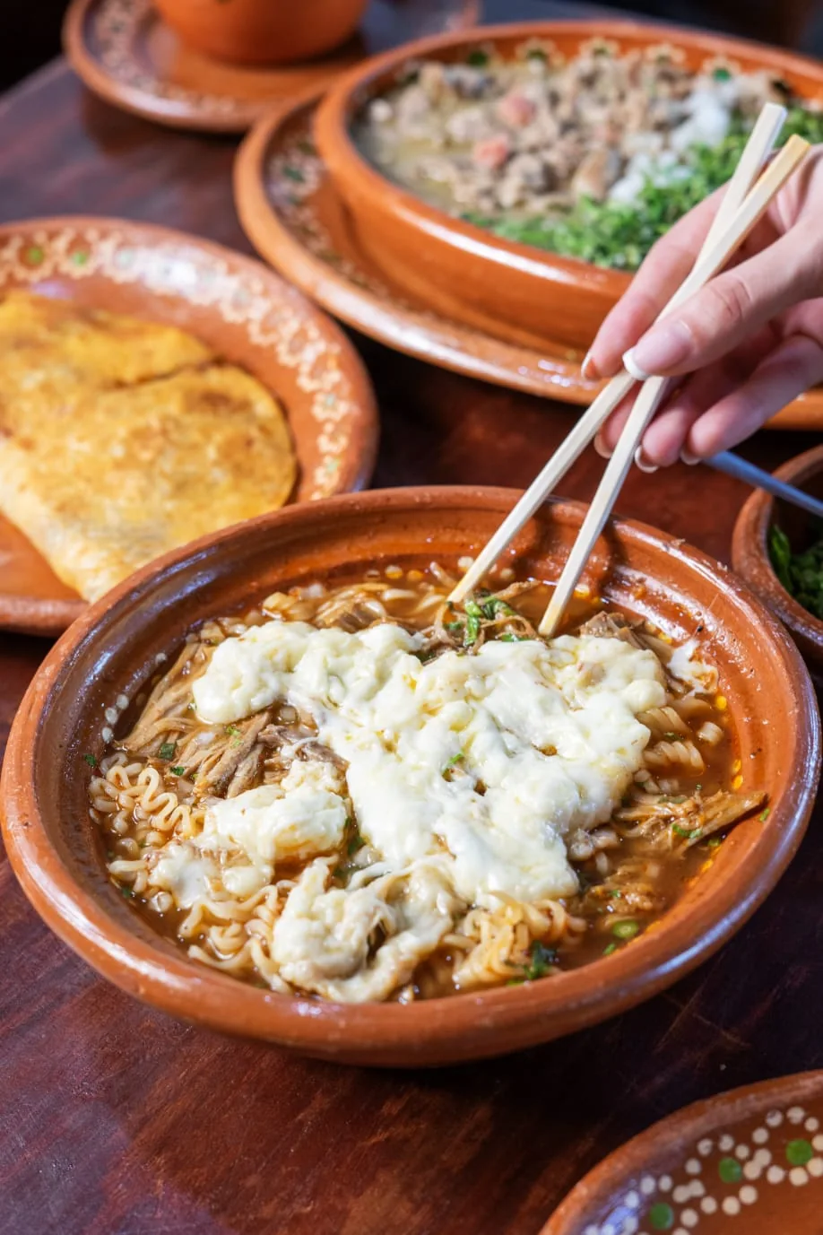 Birriamen con queso derretido, tomado con palillos.