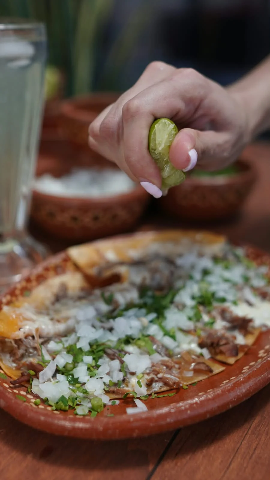 Una mano exprime limón sobre la pizzabirria.