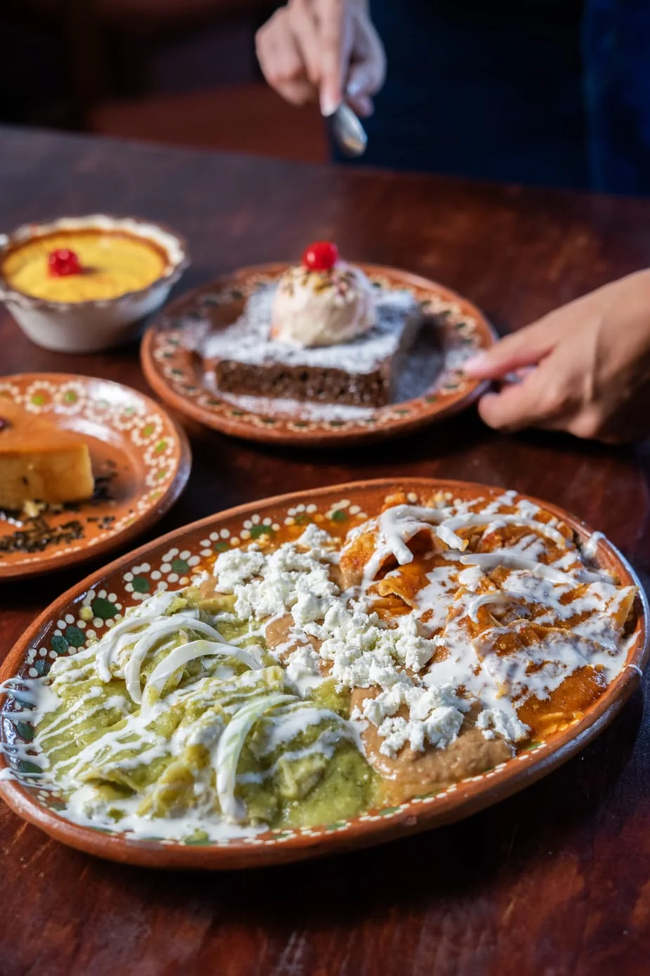 Platillo con salsa verde, crema y queso, con postres al fondo.