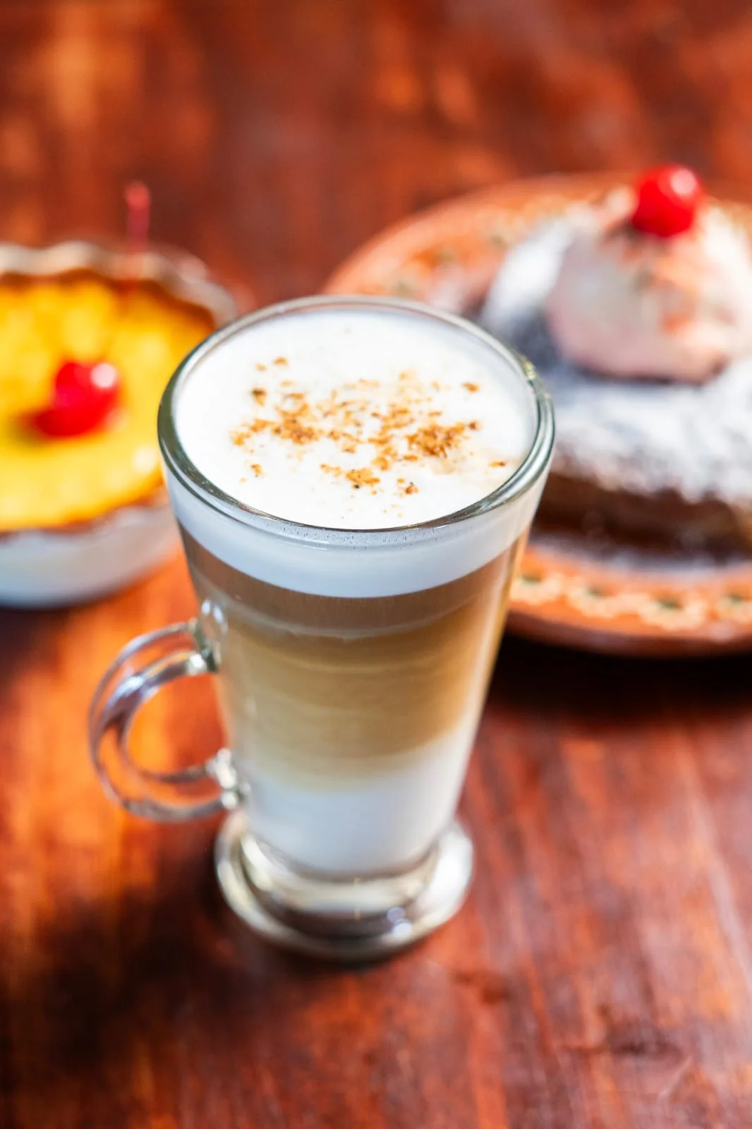 Café con leche en vaso, con postres al fondo.