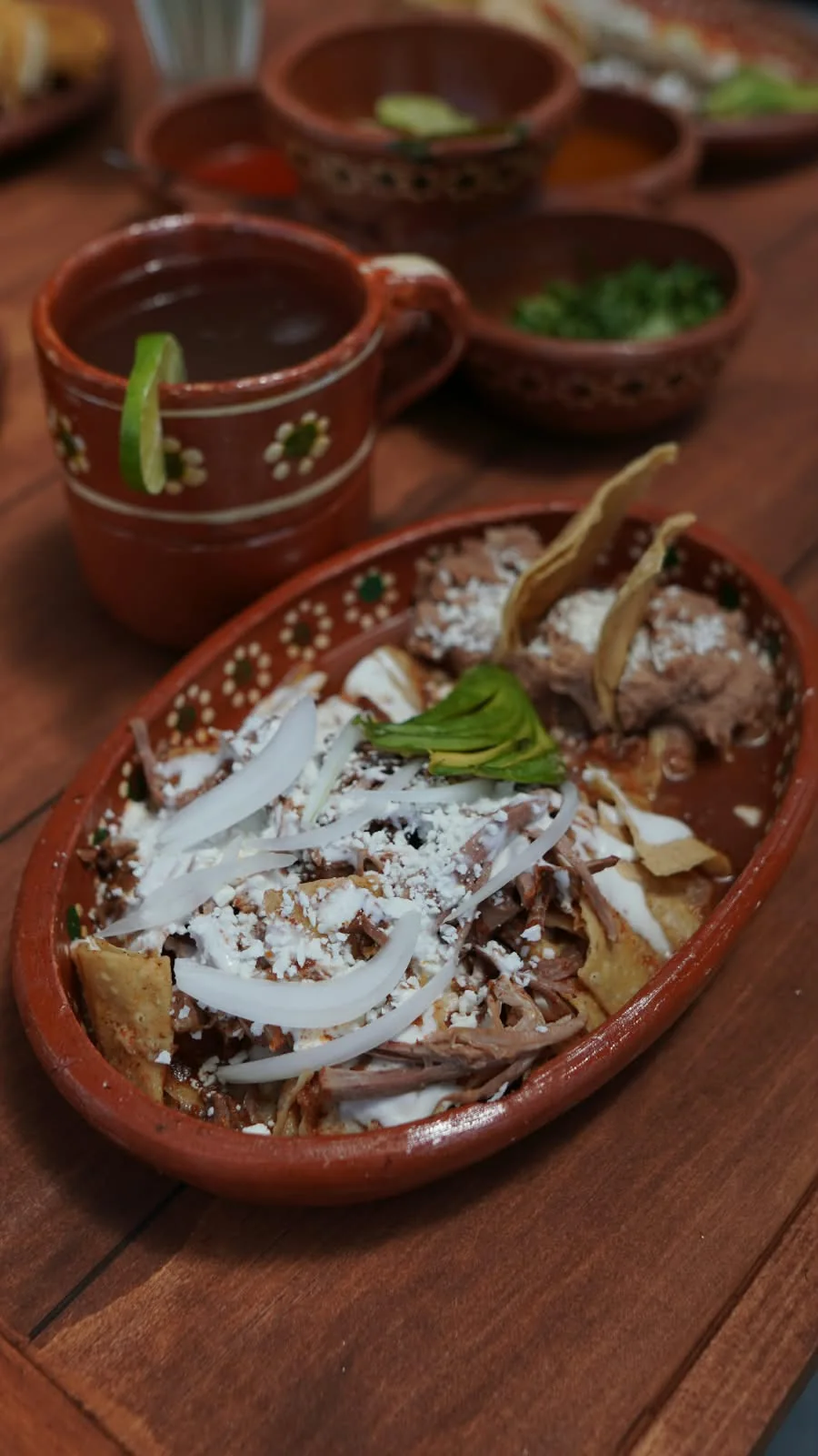 Birriaquiles con cebolla en plato de barro, con una taza de consomé.