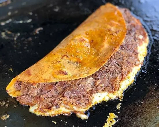 Quesabirria dorada en la plancha, con el queso saliendo por el borde.