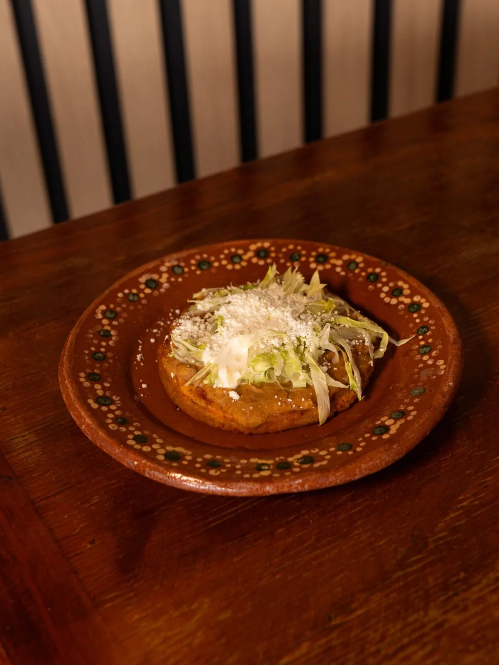 Sope con lechuga, crema y queso, en plato de barro.